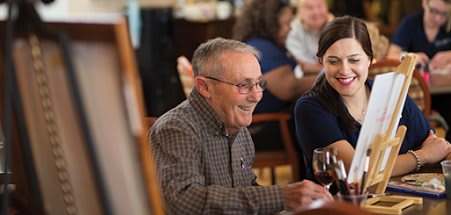 An elderly man with glasses enjoys a meal and laughs with others at a restaurant.