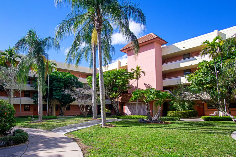 A sunny day at a tropical residential building surrounded by palm trees and a well-maintained lawn.