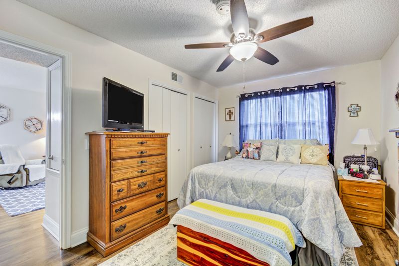 A cozy bedroom with a ceiling fan, dresser, TV, and a bed near a window with curtains.