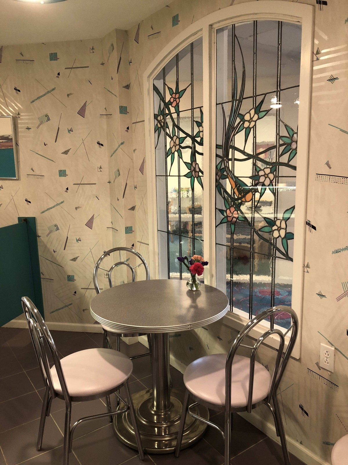 A cozy restaurant corner with a metal table, two chairs, and decorative stained glass windows.