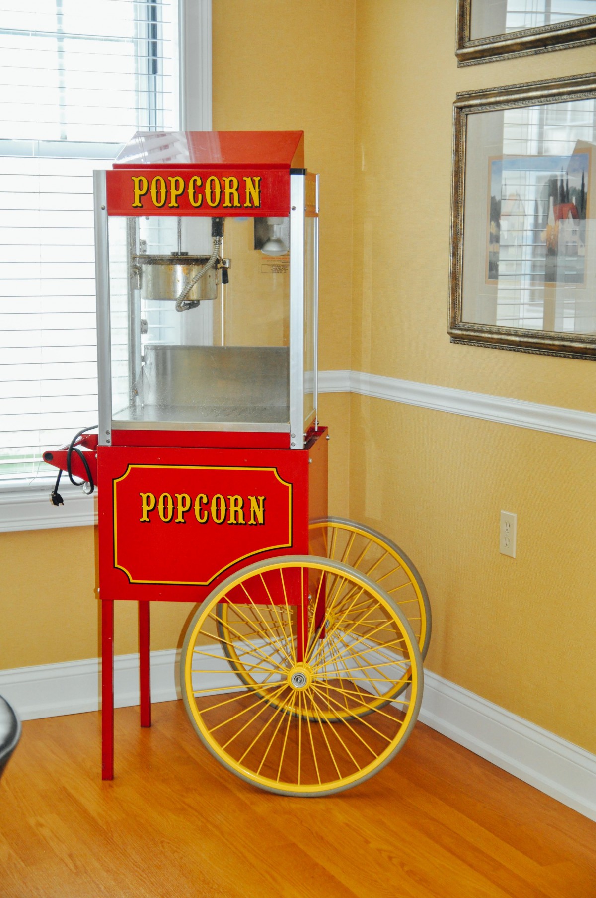 A vintage-style red popcorn machine with yellow wheels placed indoors.