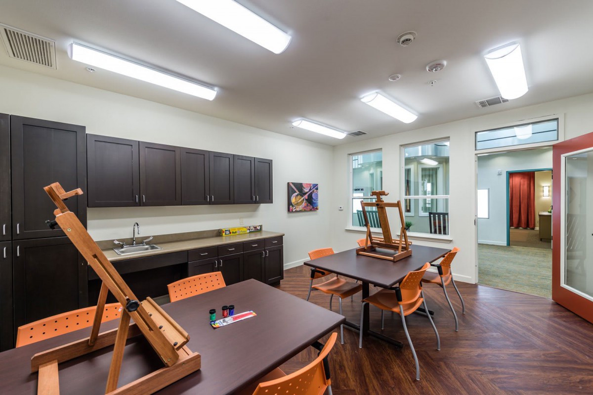 A well-lit art classroom featuring easels, tables, and cabinets stocked with art supplies.