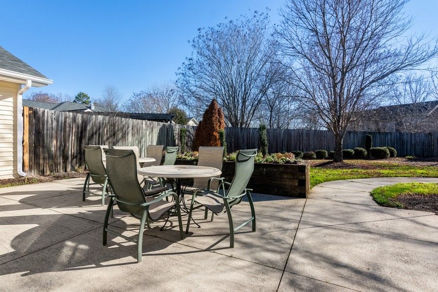 A sunny backyard patio with a table and chairs surrounded by trees.