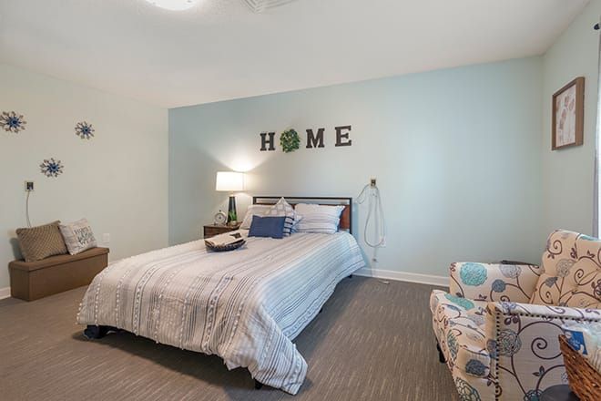 A cozy bedroom with a neatly made bed, soft lighting, and homey decorations on the wall.