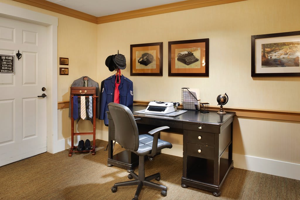 A neatly arranged home office with a desk, typewriter, and clothing rack.