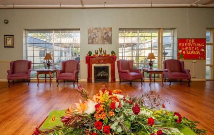 A cozy living room with a fireplace, elegant chairs, and a floral centerpiece.