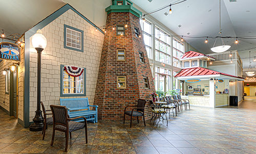 An indoor setting with a nautical theme, featuring a lighthouse structure and seating area next to large windows.