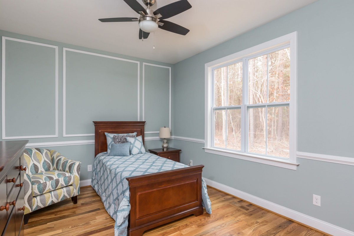 A cozy bedroom with a single bed and wooden furniture, featuring blue walls and a large window.