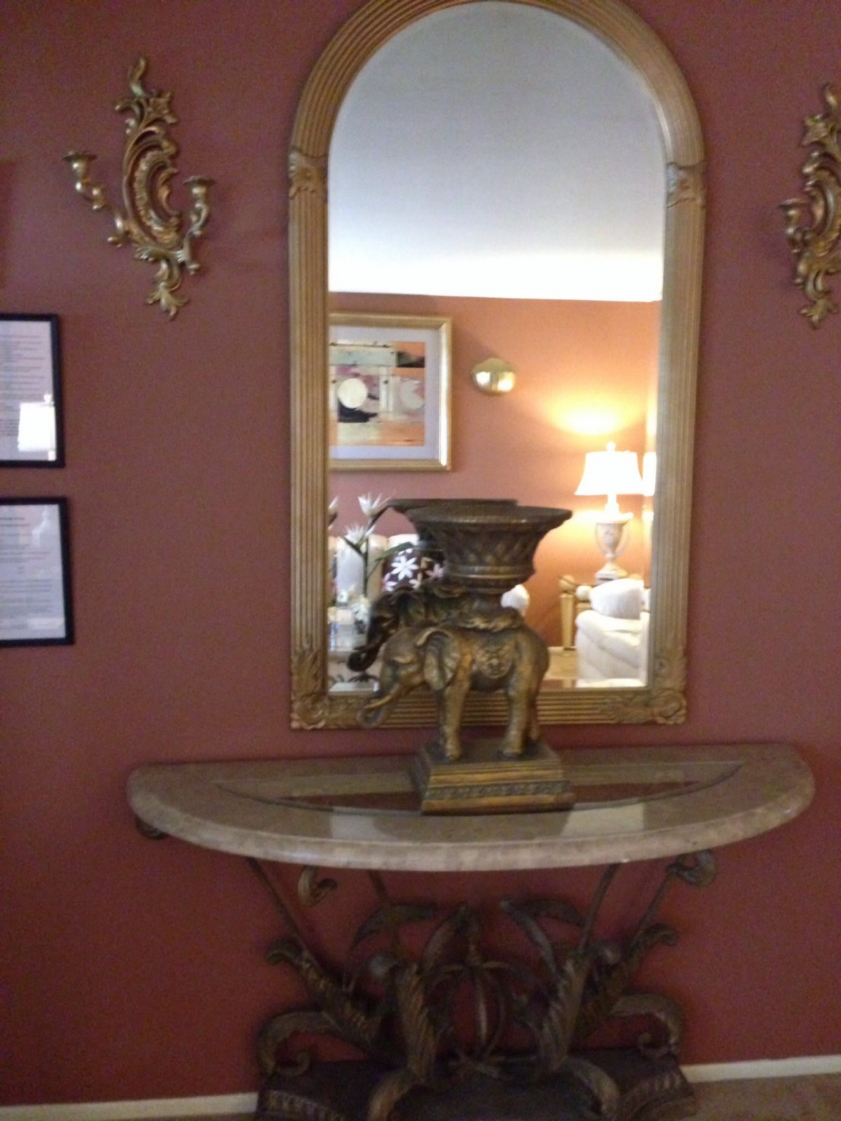 An elegant interior setup featuring a large mirror mounted above a decorative table with an ornate vase.