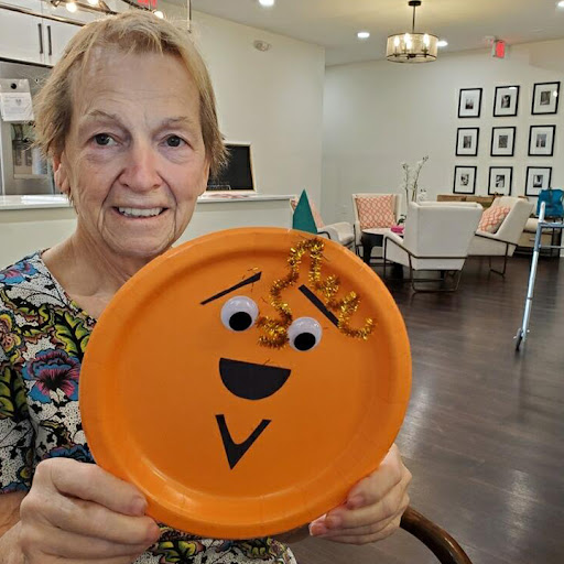 A joyful senior proudly displays her colorful craft project, showcasing creativity and fun.