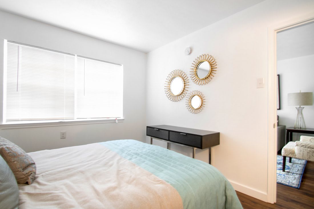 A minimalist bedroom featuring a bed, a black console table, and decorative mirrors on white walls.
