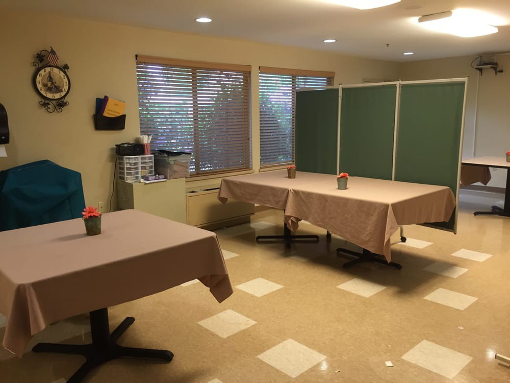 A room with tables and chairs set up, featuring windows and wall decorations.