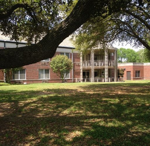 A brick building surrounded by trees with a grassy lawn.