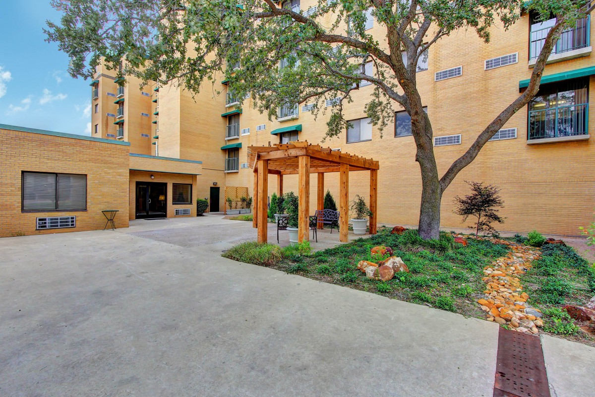 An apartment entrance with a walkway, surrounded by trees and landscaped garden.