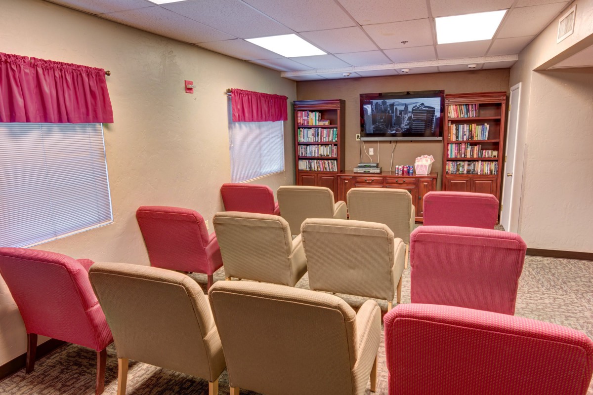 A small conference room with rows of chairs facing a television and bookshelves.