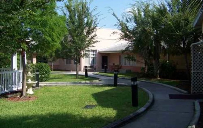A house with a surrounding yard and pathway, flanked by trees and greenery under a clear sky.