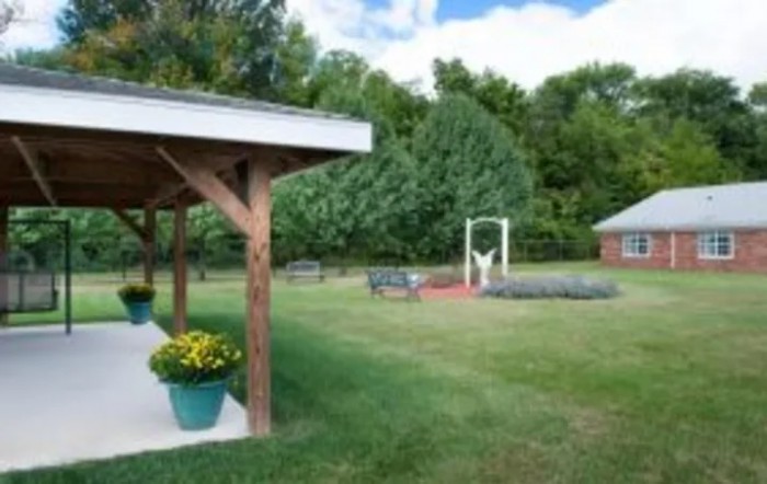 A peaceful outdoor garden area with a patio, trees, and vibrant flowers.