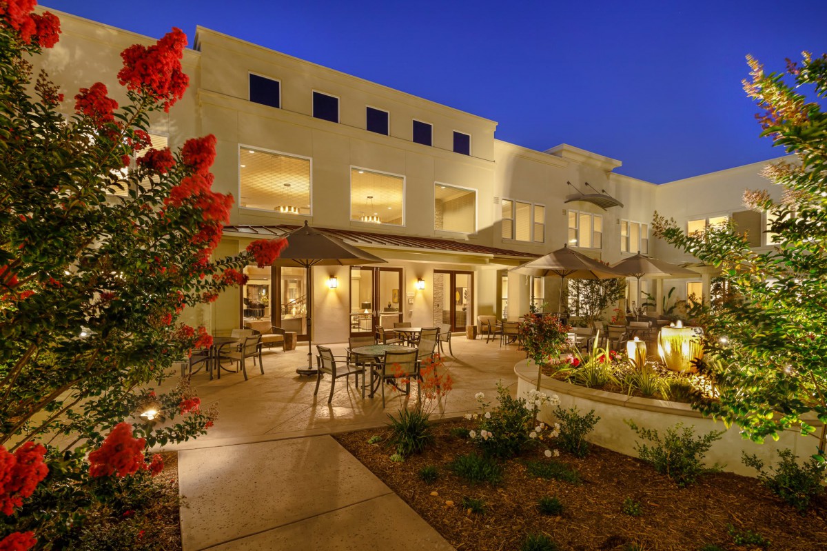 Elegant building exterior with a well-lit garden and outdoor seating area at night.