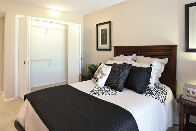 A modern bedroom with minimalist decor, featuring a neatly made bed with black and white accents and an open closet.