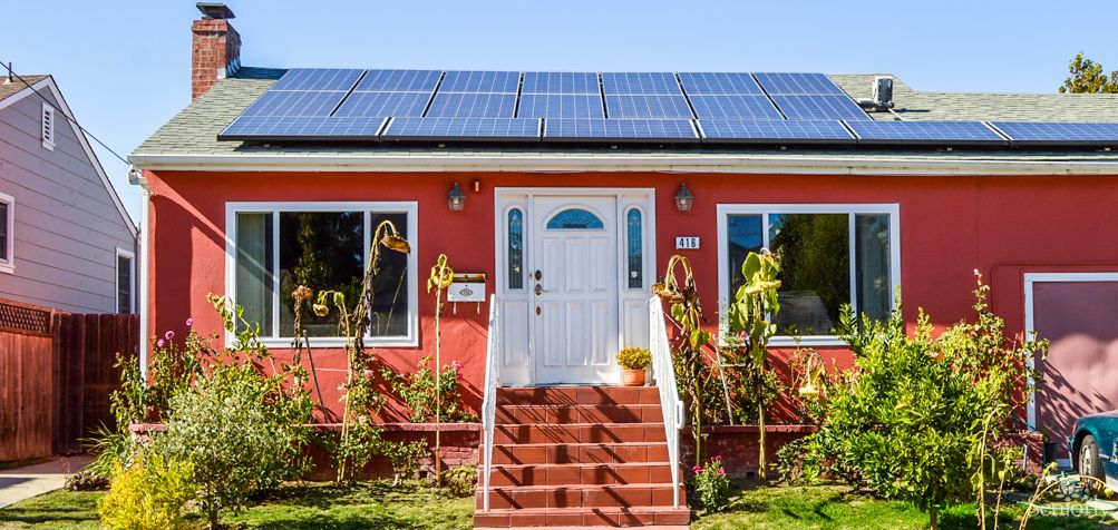 A charming red house with solar panels on the roof and a small front yard.