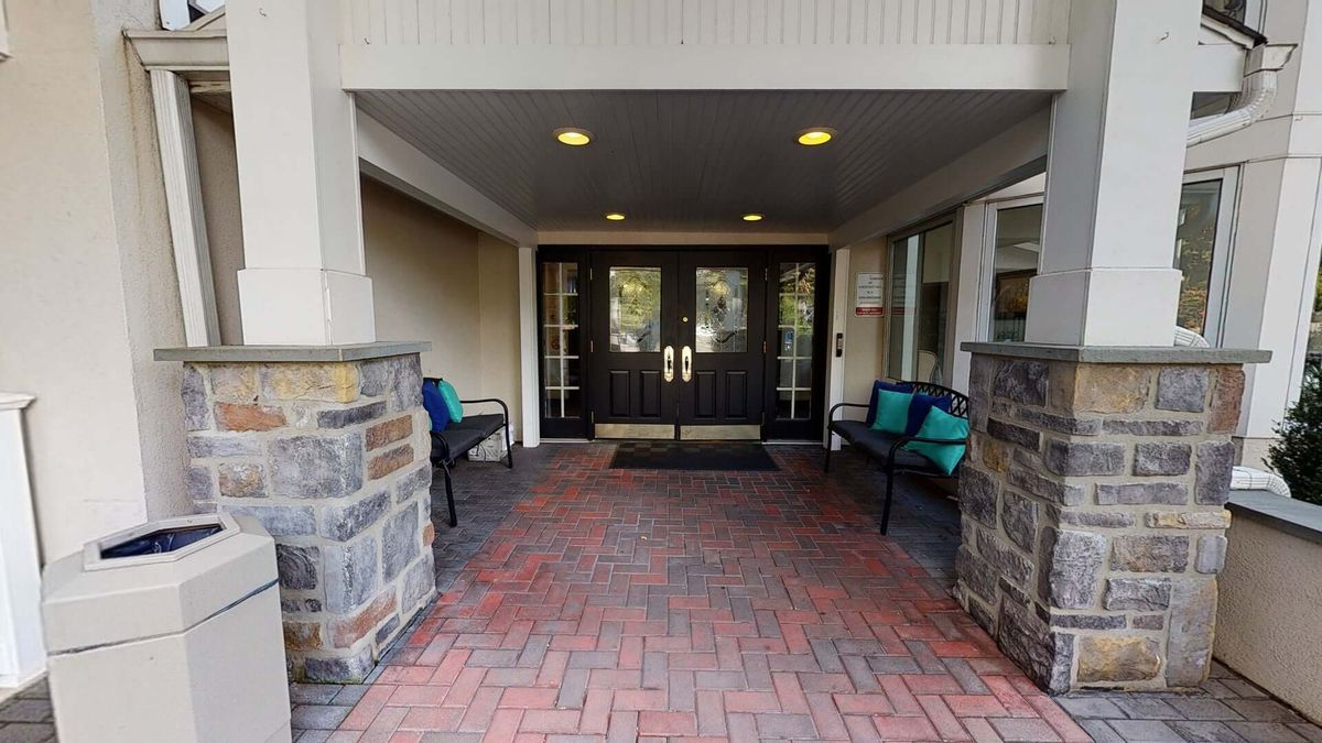 A covered entrance with double doors, brick walkway, and benches on either side.