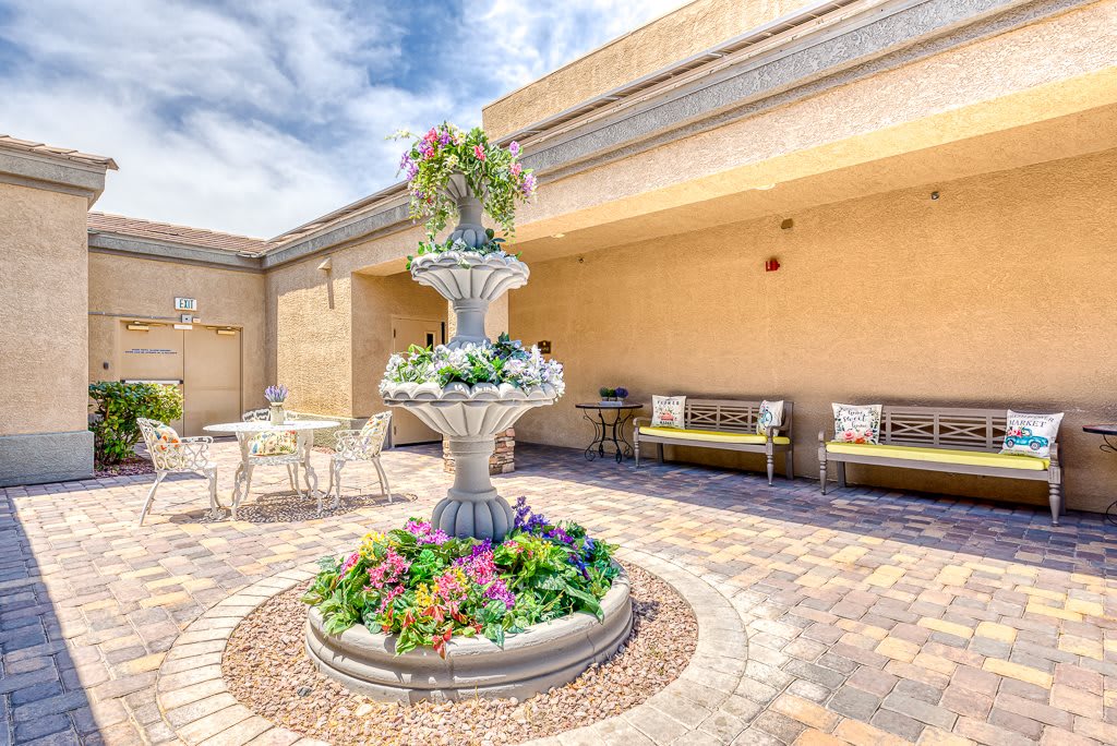 A serene courtyard featuring a decorative fountain surrounded by colorful flowers and outdoor seating.
