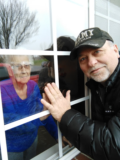A touching moment between a man and an elderly woman, sharing smiles through a window.