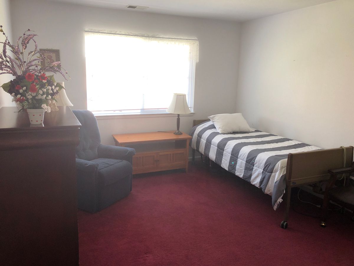 A simple bedroom with a single bed, chair, and window letting in natural light.