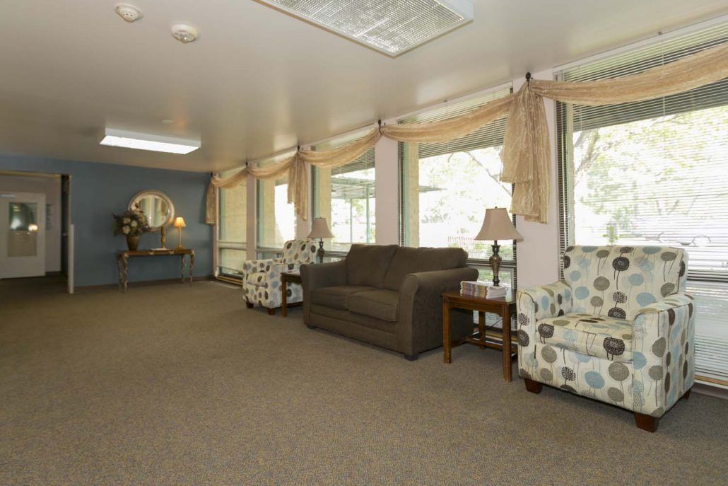 A cozy living room with a sofa, patterned chairs, and large windows with curtains.
