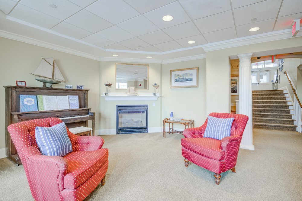 A cozy living room with bright red armchairs, a fireplace, and a piano.