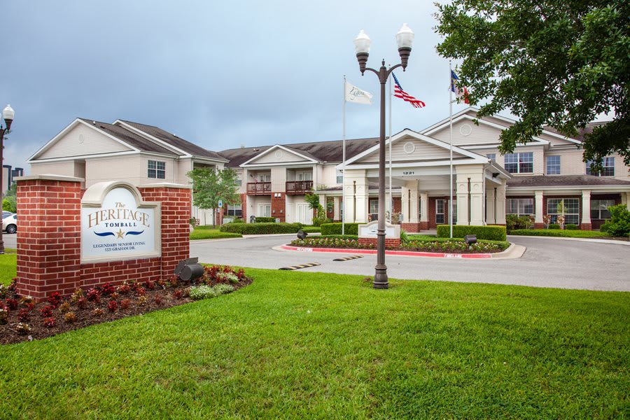 A building with an entrance sign, landscaped lawn, and flags on a cloudy day.
