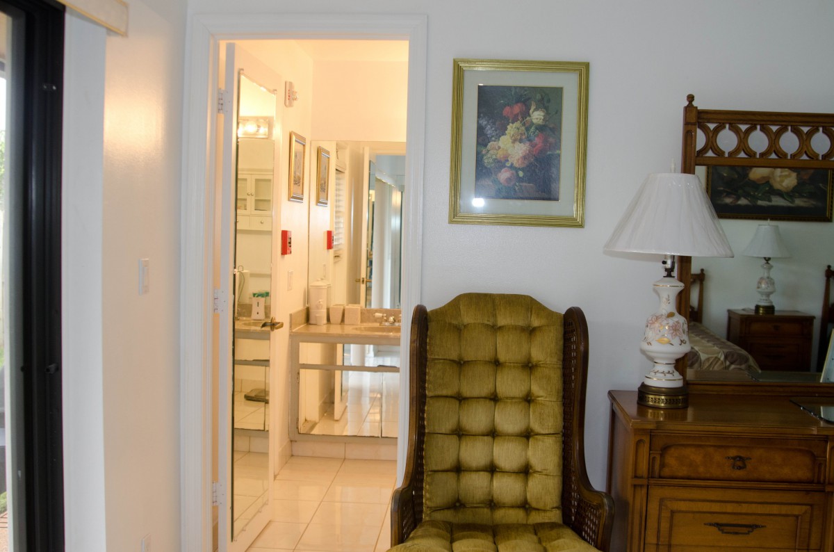 A vintage-style room with a tufted chair, artwork on the wall, and a glimpse into a well-lit hallway.