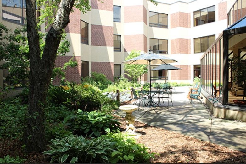 A peaceful courtyard featuring outdoor seating with tables, chairs, and umbrellas surrounded by lush greenery.