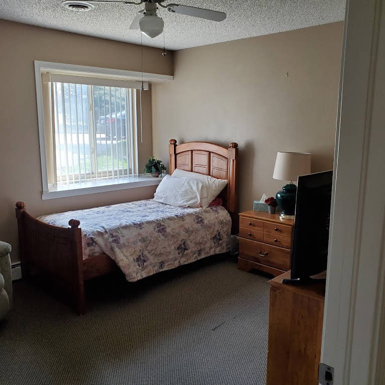 A cozy bedroom with a single bed, a window, and furniture including a lamp and TV.