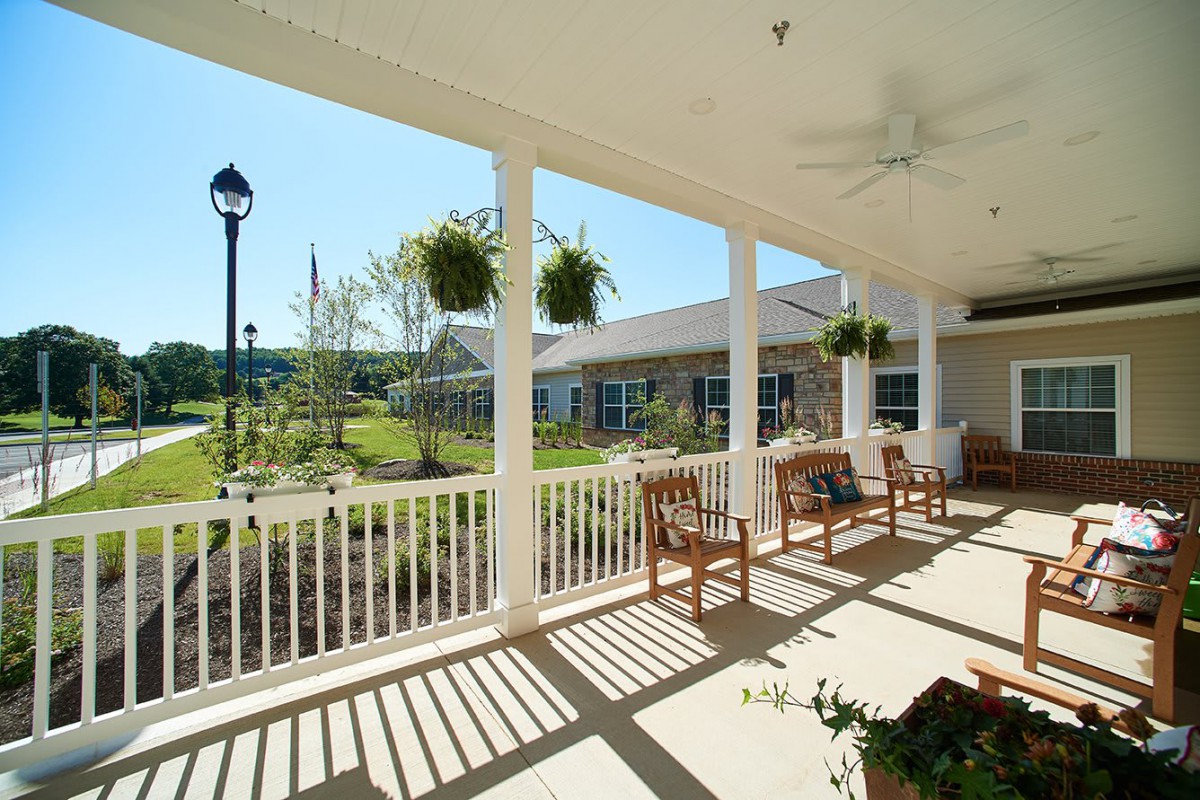 A sunny porch with benches overlooking a garden.