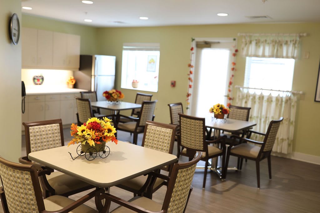 A cozy and bright dining room with neatly arranged tables and chairs, decorated with vibrant flowers.