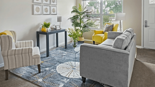 A modern living room with vibrant decor, featuring a yellow chair and a gray sofa.