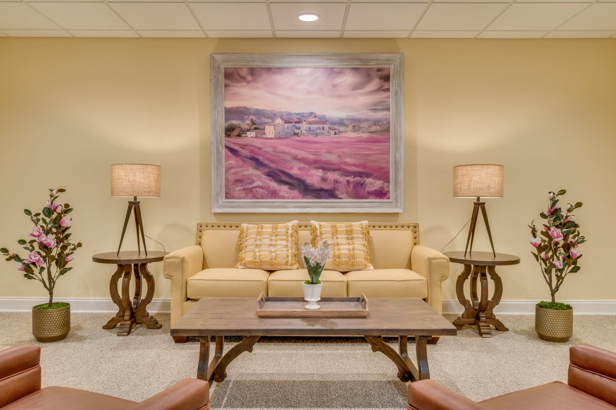 A cozy living room setting with a sofa and coffee table, adorned by two lamps and a large painting.