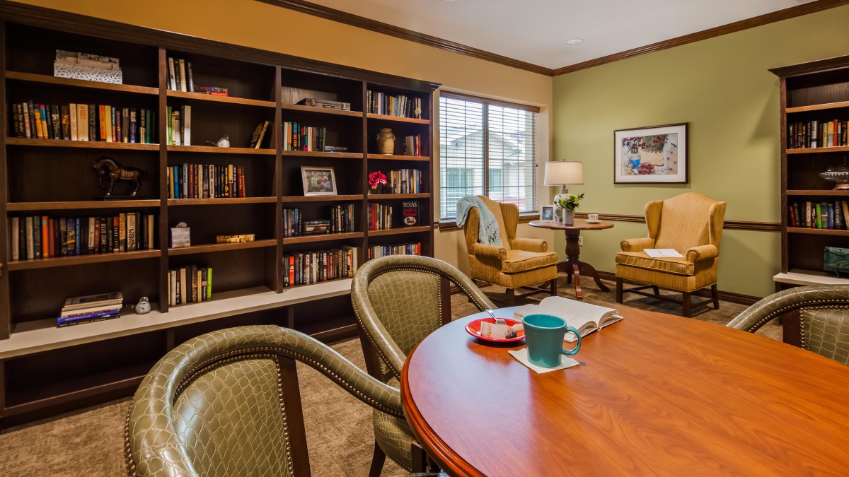 A cozy reading room with a bookshelf, table, and comfortable chairs.