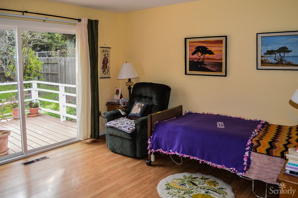 A cozy bedroom with a recliner, decorated with a purple blanket and a painting on the wall.
