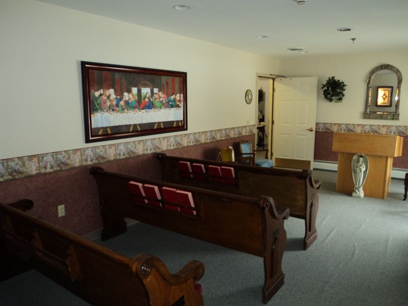 A small chapel interior with wooden pews and a religious painting on the wall.