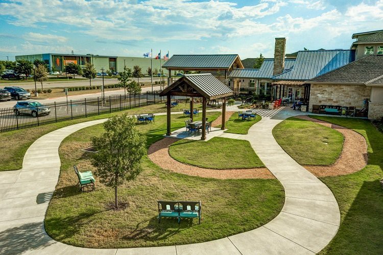 A scenic park with walking paths, benches, a pavilion, and a nearby building.