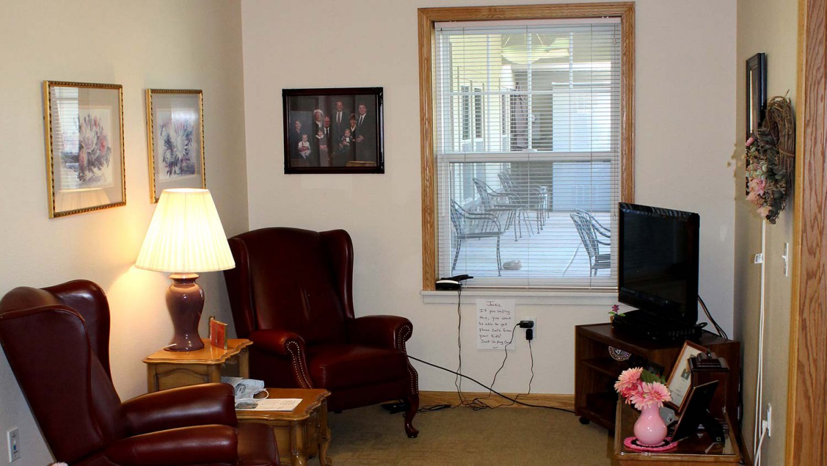 A cozy living room with armchairs, a lamp, a window, and a television.