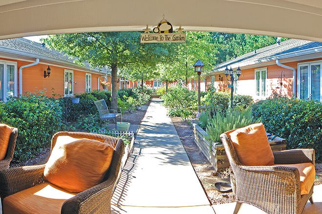 A serene courtyard with a pathway surrounded by lush gardens and outdoor seating.