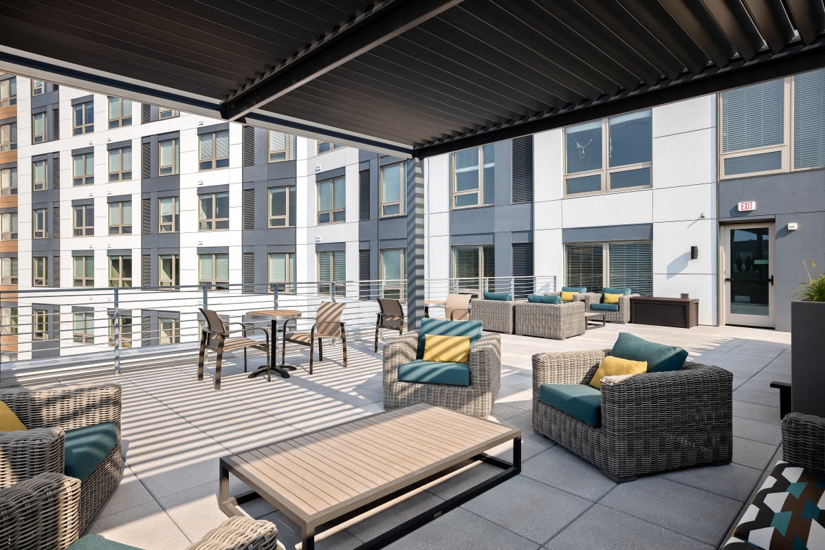 A modern outdoor patio with comfortable seating and tables in an urban apartment setting.