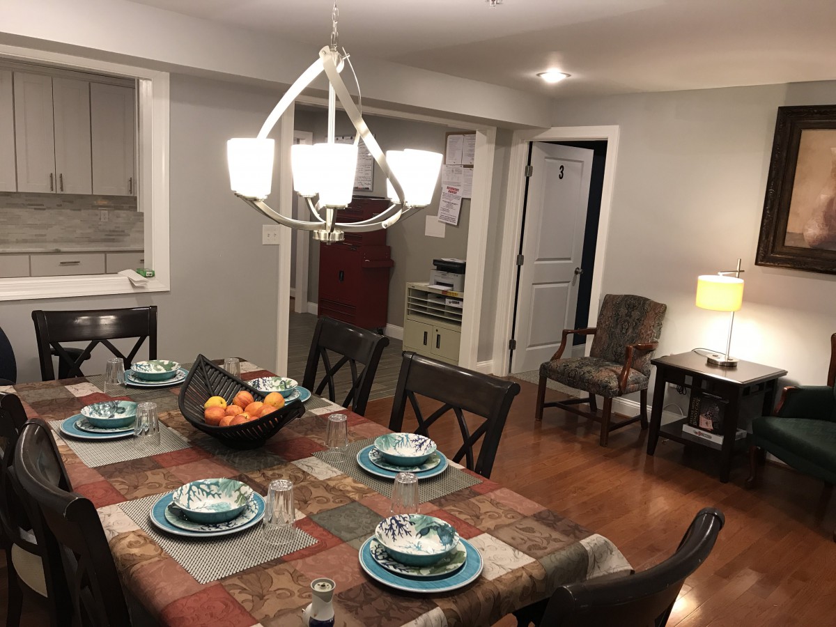 A well-set dining table in a cozy dining room featuring elegant dinnerware and a central fruit bowl under a modern chandelier.