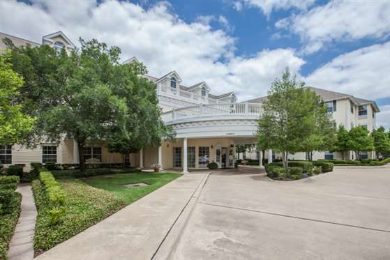 A building with a grand entrance surrounded by greenery under a partly cloudy sky.