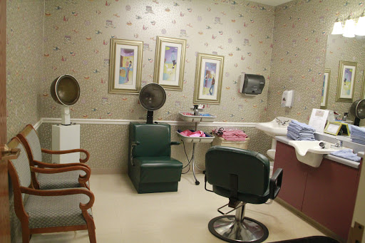 A cozy hair salon interior featuring a green chair, framed artwork, and salon equipment.