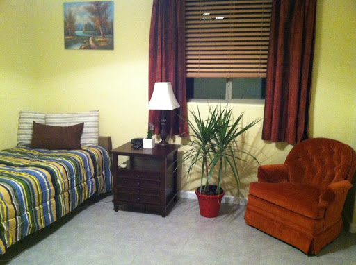 A cozy bedroom featuring a striped bedspread, a bedside lamp, and an orange chair.