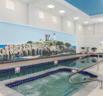 An indoor swimming facility featuring a hot tub and a wall mural of a coastal scene.
